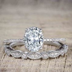 an oval shaped diamond ring on top of a wooden table with two matching wedding bands