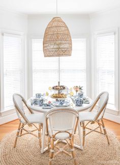 a dining room table with chairs and plates on it in front of two large windows