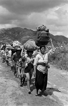 a group of people walking down a dirt road with bags on their heads and luggage on their shoulders