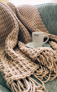 a coffee cup is sitting on a couch with a knitted blanket around it and the words muk written in white