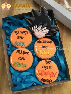 four decorated cookies in a box with blue ribbon around the edges and an image of goku