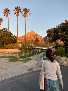 a woman is walking down the street with her hand up in the air and palm trees behind her