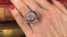 a close up of a person's hand with a ring on their finger and books in the background