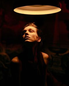 a woman standing under a lamp in the dark with her eyes closed and head turned to the side