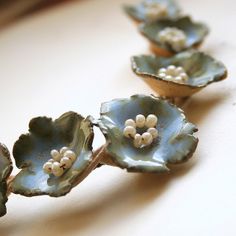 three blue flower shaped dishes sitting on top of a white tableclothed surface with pearls in the center