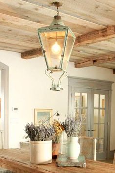 a wooden table topped with two vases filled with flowers next to a light fixture