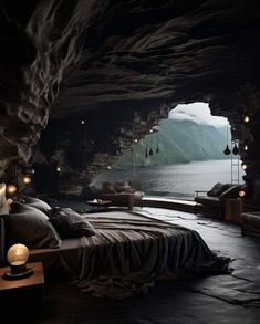 a bed sitting in the middle of a cave next to a body of water with mountains in the background