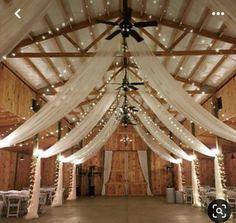 the inside of a barn decorated with white drapes and lights