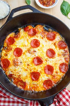 a pepperoni pizza in a skillet on a table next to other food items