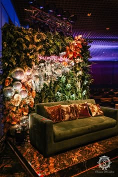 a green couch sitting in front of a wall covered with plants and balls on top of a table