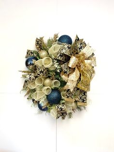 a christmas wreath with blue and gold ornaments on white wall behind the wreath is an ornament