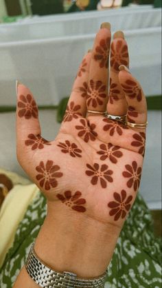 a woman's hand with brown flowers painted on it and two rings around her wrist