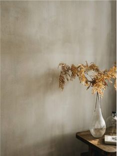 a vase filled with flowers sitting on top of a wooden table next to a wall