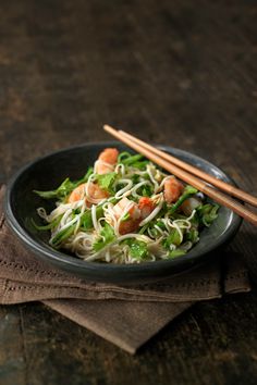 a black bowl filled with noodles and shrimp next to chopsticks on top of a napkin