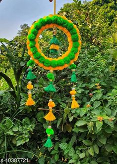 a green and yellow wreath with tassels hanging from it's center surrounded by greenery