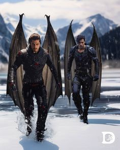 two men dressed in black are walking through the snow with wings on their back and feet