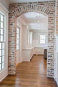 an empty room with wood flooring and brick arches on the wall, along with windows