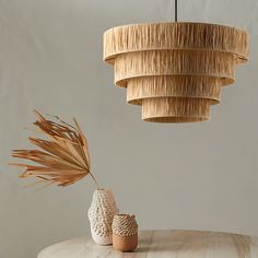 two vases sitting on top of a wooden table next to a light hanging from the ceiling