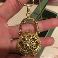 a hand holding a gold purse shaped pendant