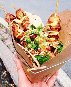 a person holding up a paper container filled with food on top of a street corner