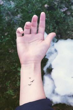 a person's hand with a small bird tattoo on their left wrist and the sky in the background