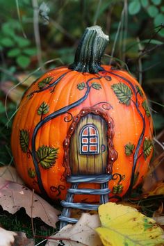 a painted pumpkin sitting in the grass with leaves around it and a house on top