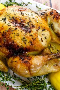 a whole chicken on a plate with lemons and herbs