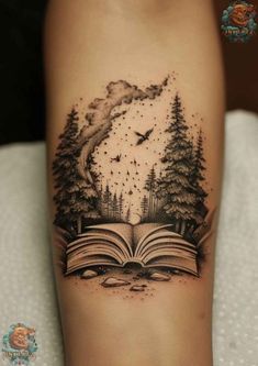 an open book tattoo on the arm with trees and birds flying over it, in front of