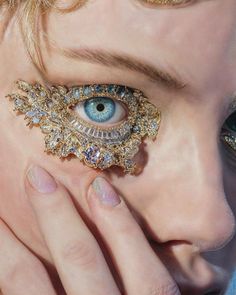 a close up of a person's eye with gold jewelry on their fingers and an eyeball in the middle