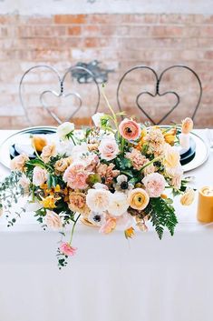 an arrangement of flowers in a vase on a white tablecloth with chairs behind it