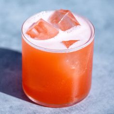 an orange drink in a glass with ice cubes on the rim, sitting on a gray surface