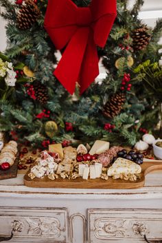 an assortment of cheeses and crackers on a wooden cutting board in front of a christmas tree