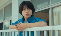 a young boy standing on a porch with his arms crossed and looking out the window