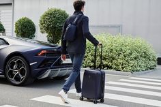 a man walking across the street with a suitcase next to a sports car and bushes