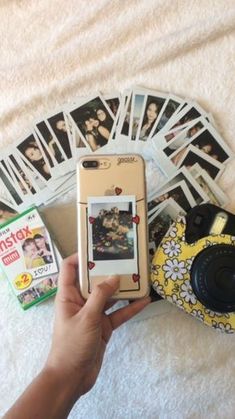 a person holding a cell phone in their hand with pictures on the table behind them