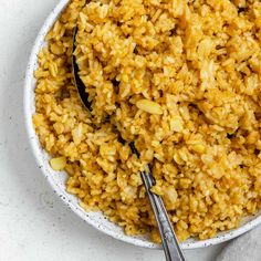 a white bowl filled with yellow rice and two spoons on top of the bowl