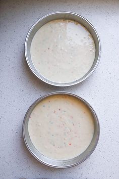 two metal pans filled with batter sitting on top of a white counter next to each other