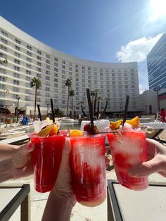 two people hold up glasses with drinks in front of a hotel pool and palm trees