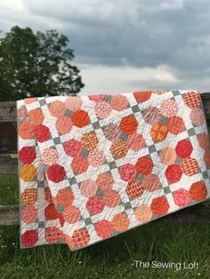 an orange and grey quilt hanging on a wooden fence in the middle of a field