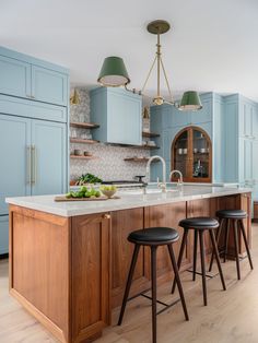 a kitchen with blue cabinets and stools next to an island in the middle of the room