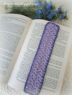 an open book with a crocheted cover on top of it next to a blue flower