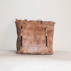 This rustic, leather travel tote is ideal for organizing your belongings on the go. Its brass brads, double exterior pocket, exterior conceal and carry pocket, interior double pocket, interior zipper pocket, and lined interior provide generous space for all your essentials. The perfect blend of functionality and style. About 11” x 14” Shipping on custom items takes 8-10 business days. Everyday Rugged Bag With Leather Handles, Rugged Everyday Bag With Leather Handles, Rugged Leather Satchel For Everyday Use, Rugged Leather-backed Satchel For Everyday, Rugged Soft Leather Bag For Daily Use, Rugged Shoulder Bag For Travel, Vintage Leather Backpack With Zipper For Everyday Use, Rugged Everyday Bags With Leather Lining, Rugged Everyday Bag With Leather Lining