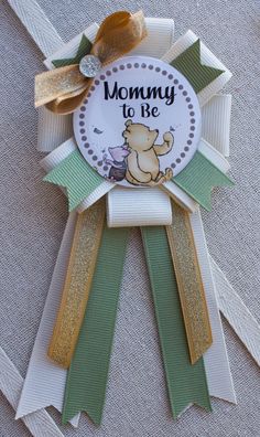 there is a ribbon that says mommy to be with a bear on it and gold bow