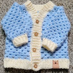 a blue and white crocheted sweater laying on the floor next to a brown teddy bear