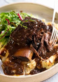 a white plate topped with meat and potatoes covered in gravy next to a salad