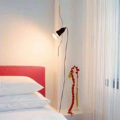 a bed with white sheets and pillows next to a red headboard on the wall