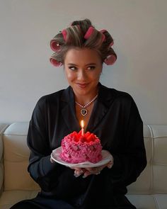 a woman sitting on a couch holding a cake with candles in her hair and looking at the camera