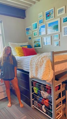 a woman standing next to a bed in a room with lots of pictures on the wall