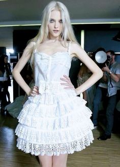 a woman in a white dress standing on a wooden floor with her hands on her hips