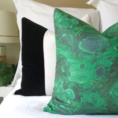 a green pillow sitting on top of a bed next to two black and white pillows